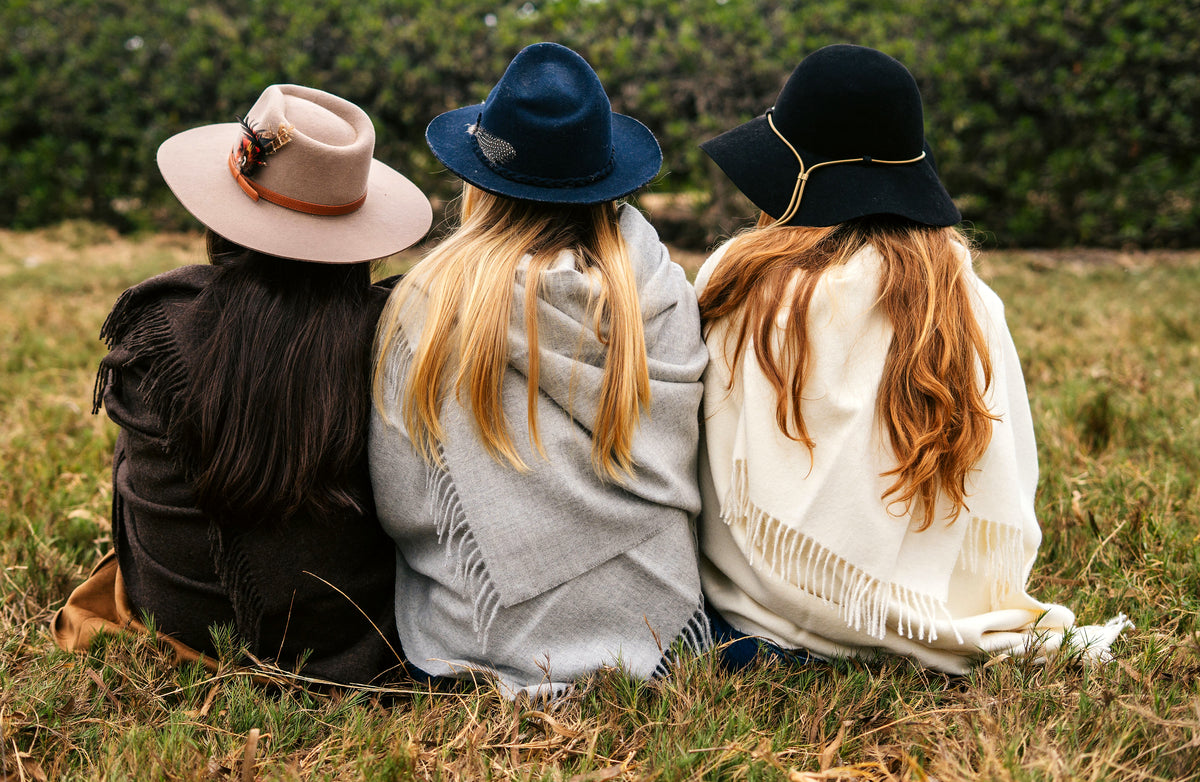 Three women sitting in a field in Peru, wrapped in Andean, Sterling and Natural baby alpaca throws