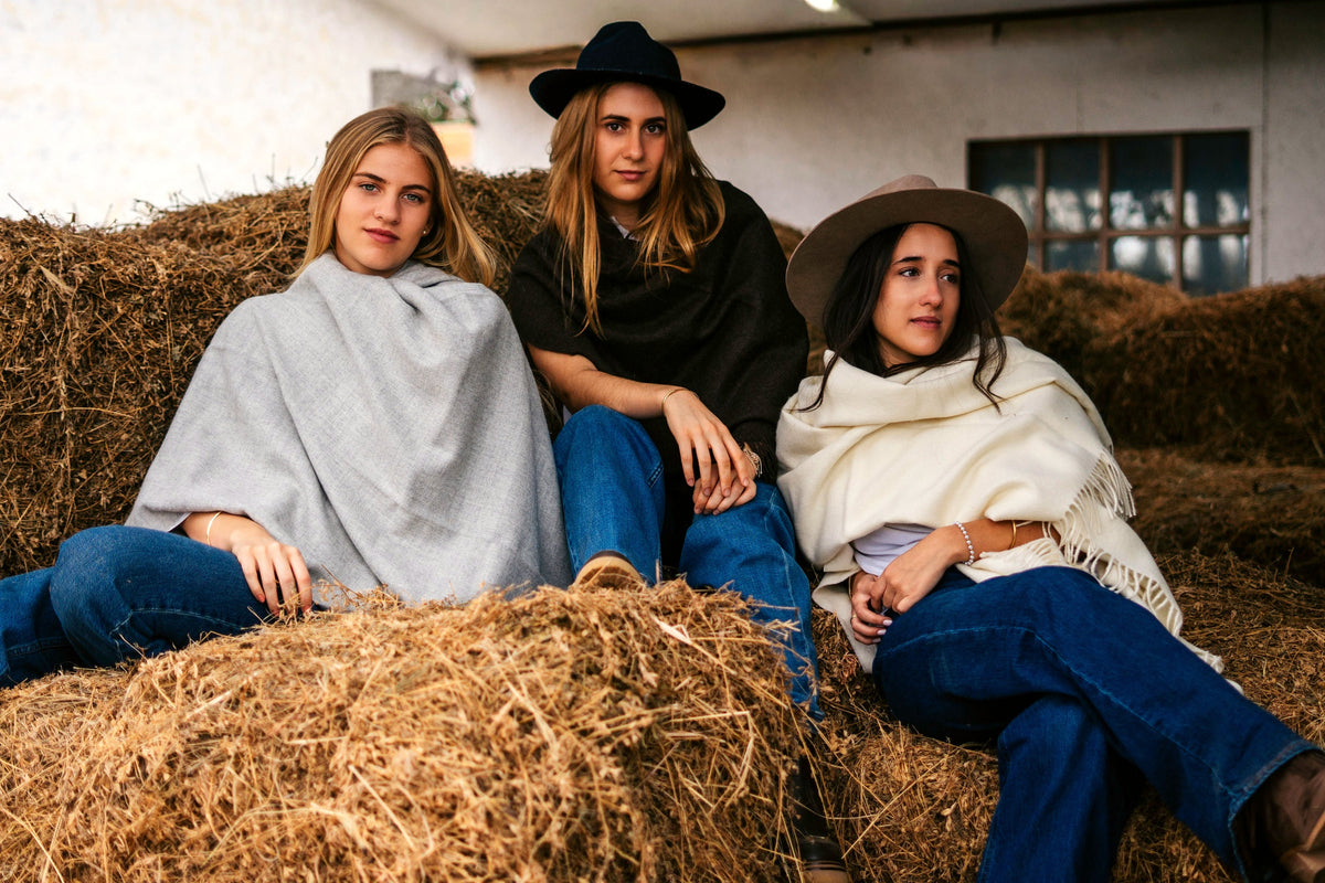 Three models on hay bales wearing the Storm, Vicuña, and Natural throws