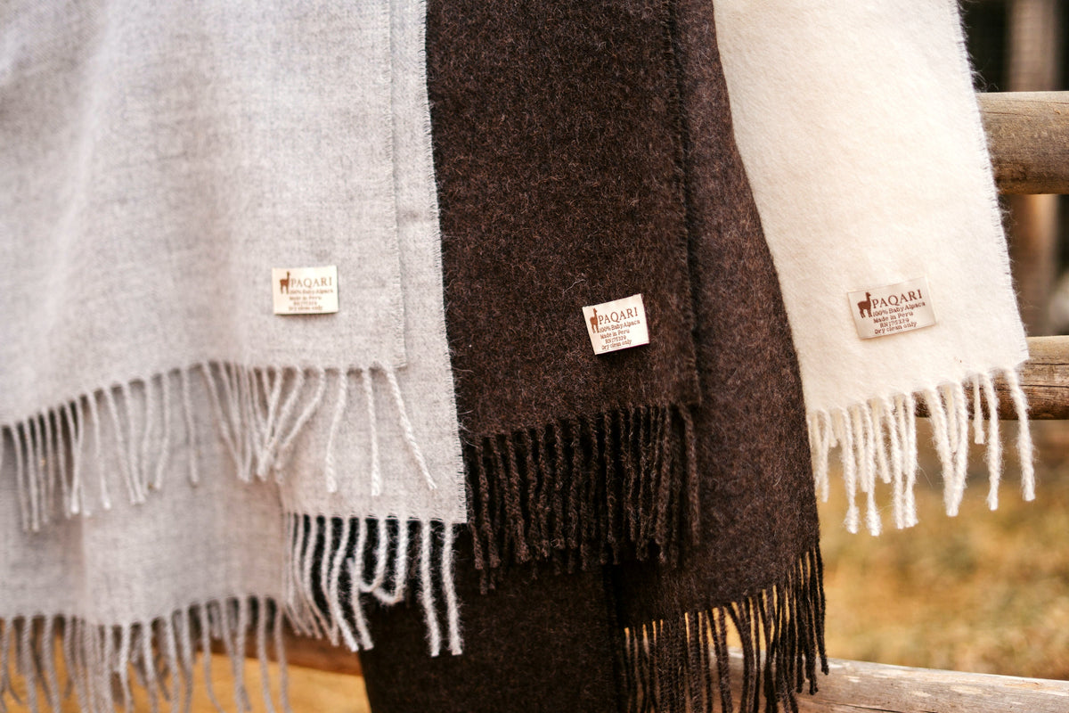 Storm, Vicuña, and Natural throws stacked, PAQARI woven labels visible