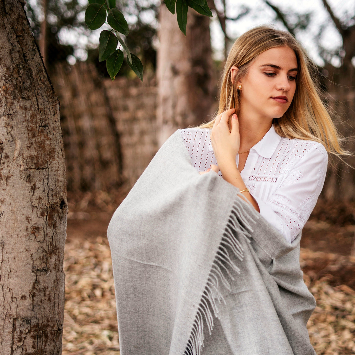 Model standing wrapped in the Storm grey throw beside eucalyptus wood