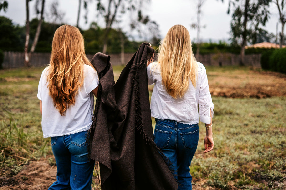 Two models carrying the Andean brown baby alpaca throw through a Peruvian field