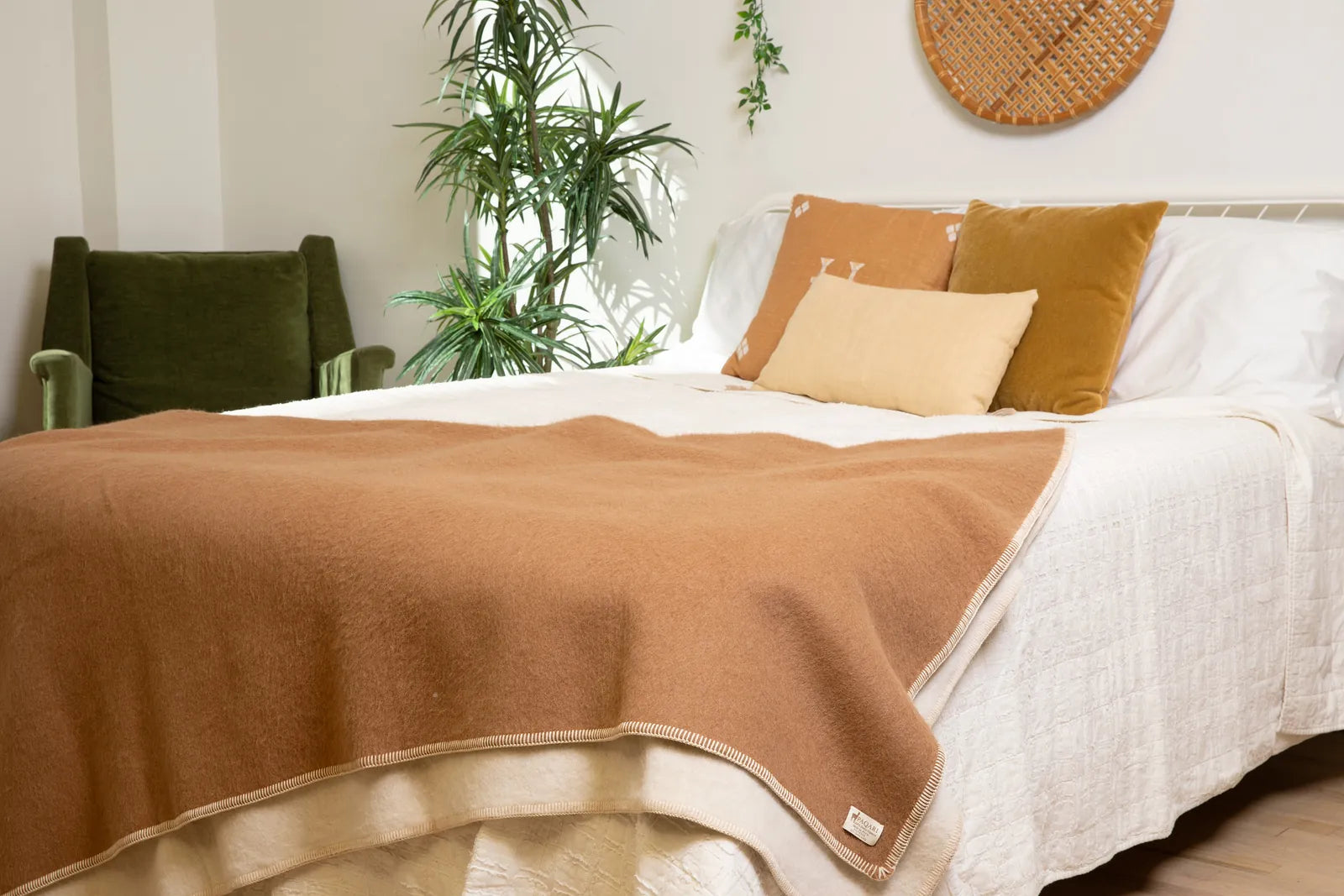 Camel side of the Paqari blanket draped over the foot of a bed, with the cream stitched edge and corner tag visible